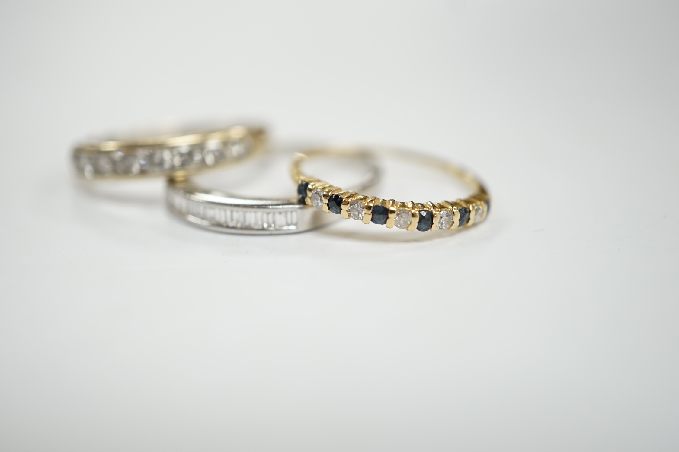 A white metal (stamped 950) and thirteen stone channel set baguette cut diamond ring, size O, together with two other unmarked gem set rings including diamond half eternity ring.
